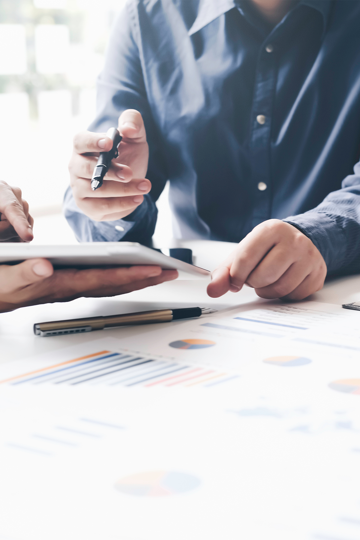 Two people in business attire review data charts and graphs on a table, using a tablet and pens.