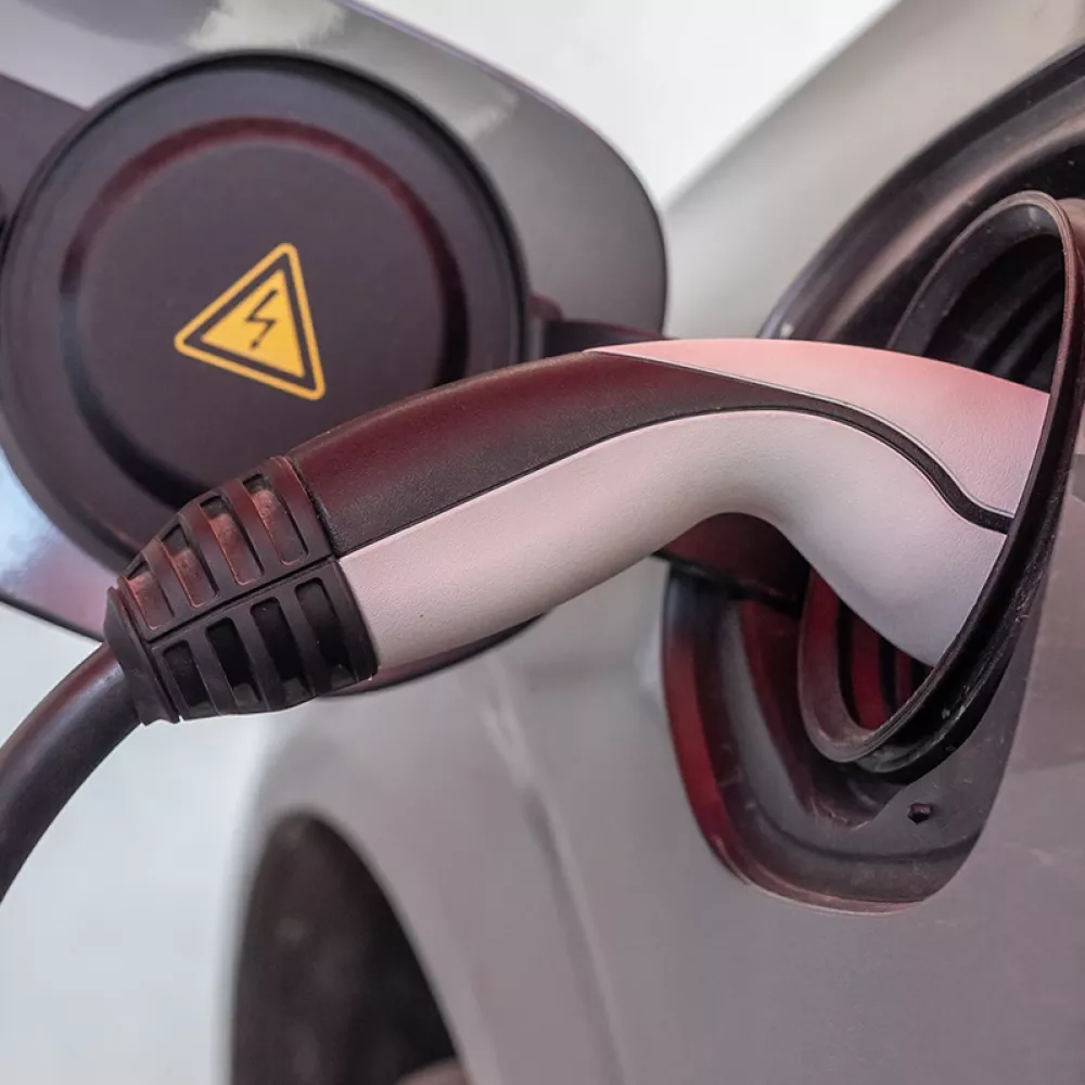 Close-up of an electric car charging connector plugged into the vehicle’s charging port, with a high-voltage warning symbol visible.