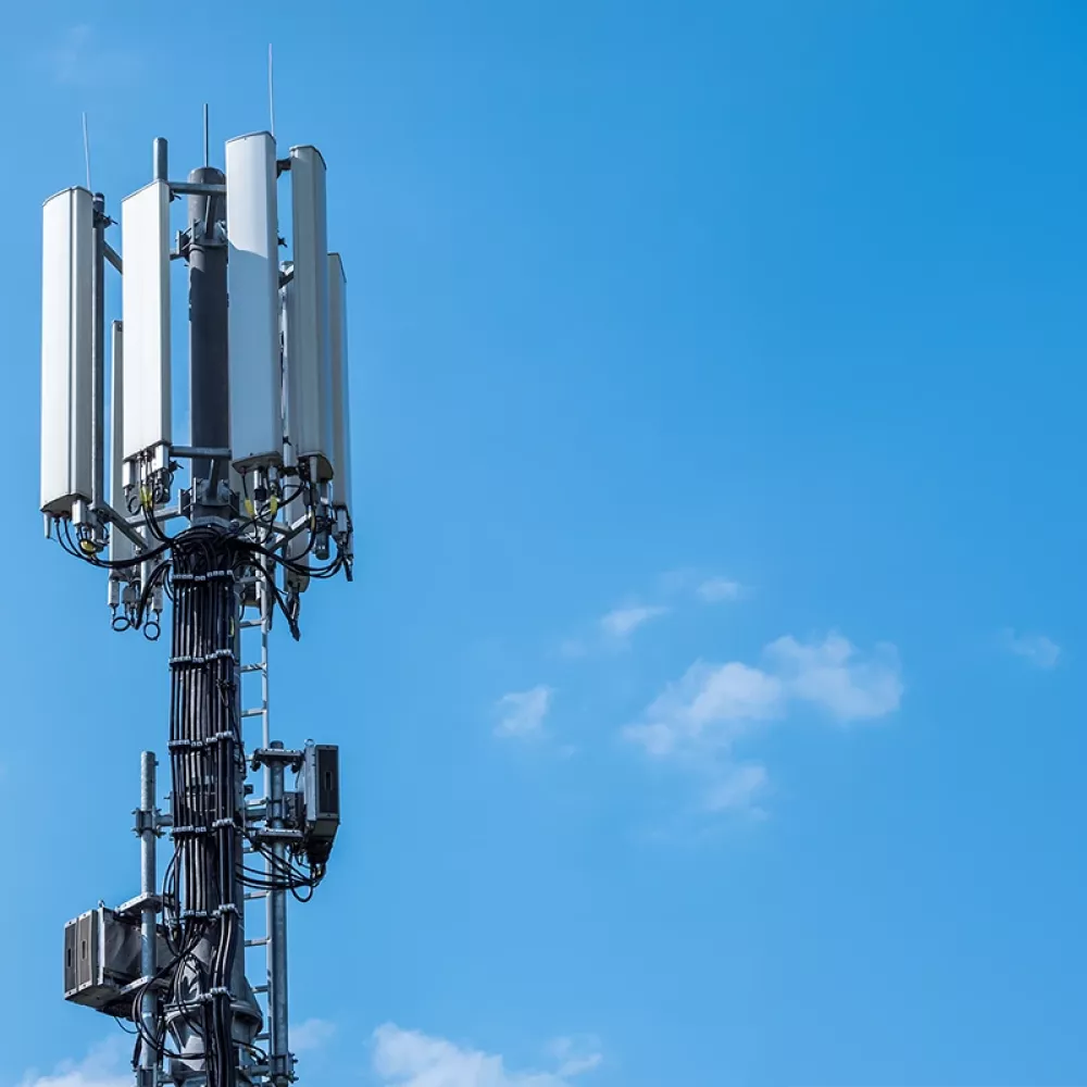 Cellular base station tower with multiple antenna panels and cables against clear blue sky.